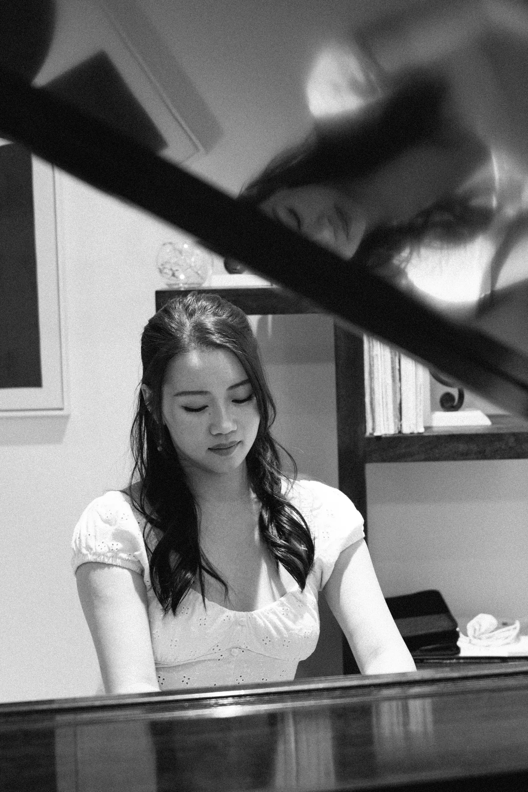 Beverly Wang at a grand piano, reflected in the raised lid
